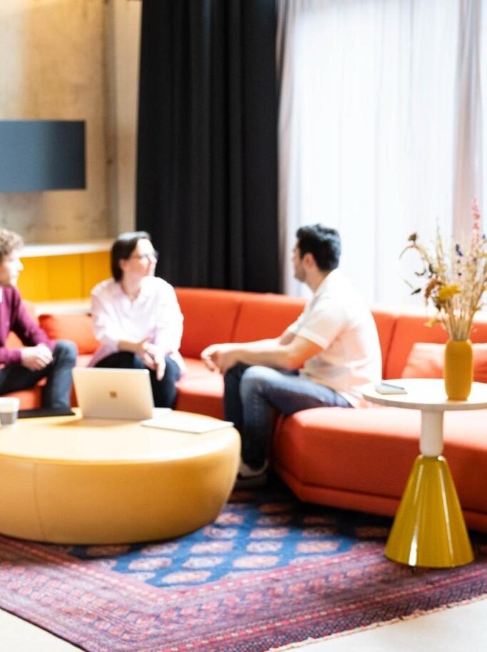 Drei verschwommene Personen sitzen auf einer Couch und unterhalten sich.