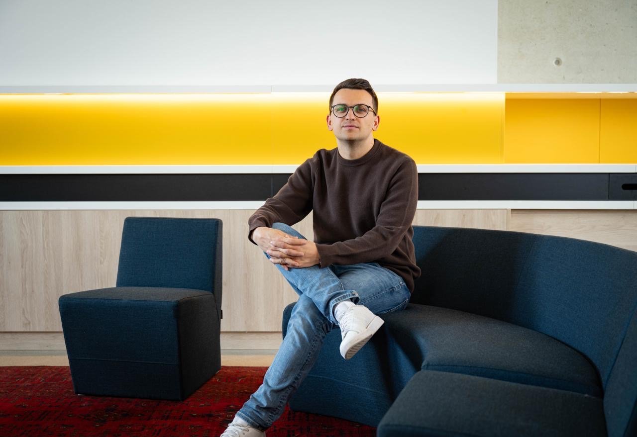 Mann sitzt auf einem blauen Sofa und schaut in die Kamera