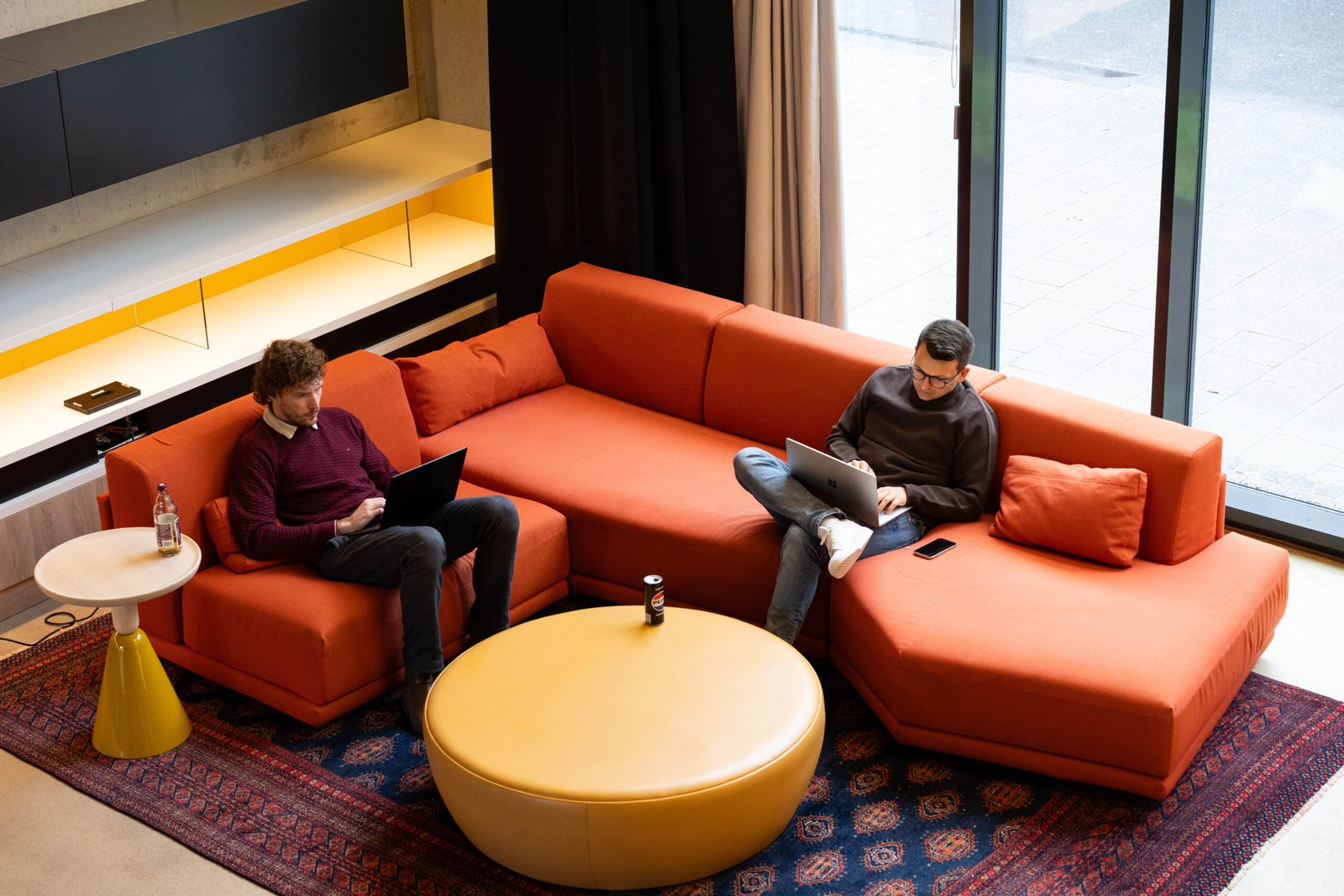 Vogelperspektive: Zwei Menschen sitzen auf einem roten Sofa und arbeiten am Laptop