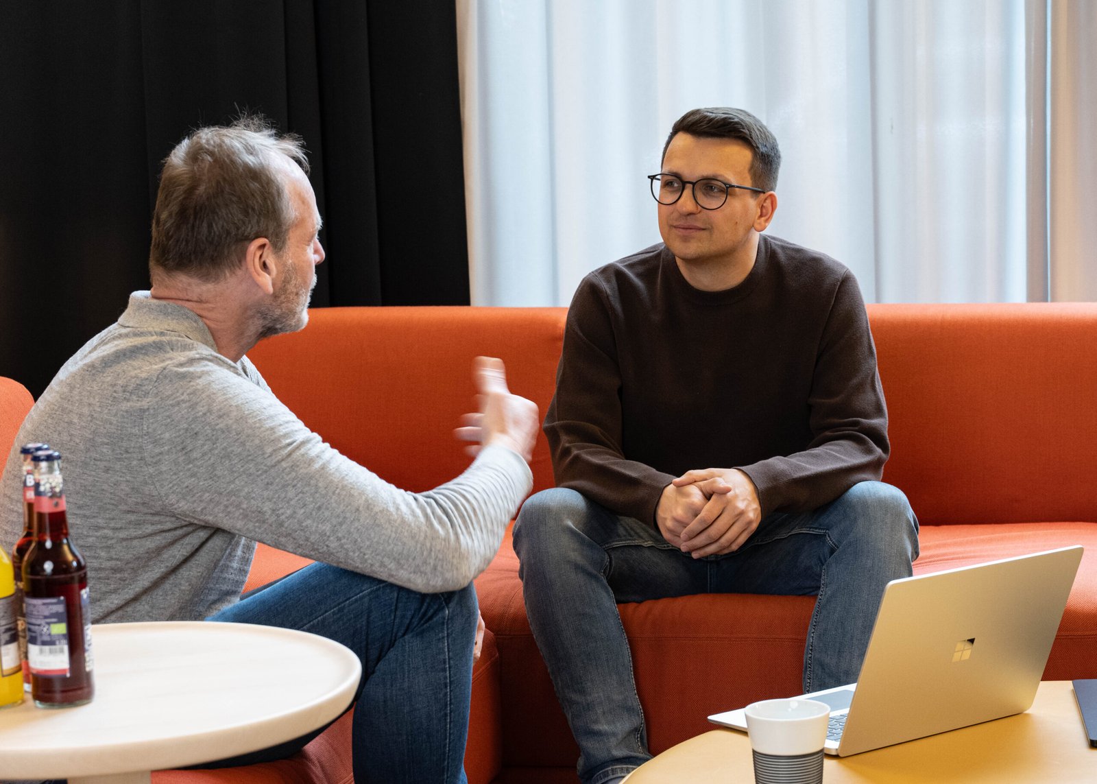 Zwei Männer sitzen auf einem roten Sofa und unterhalten sich über Marketing.