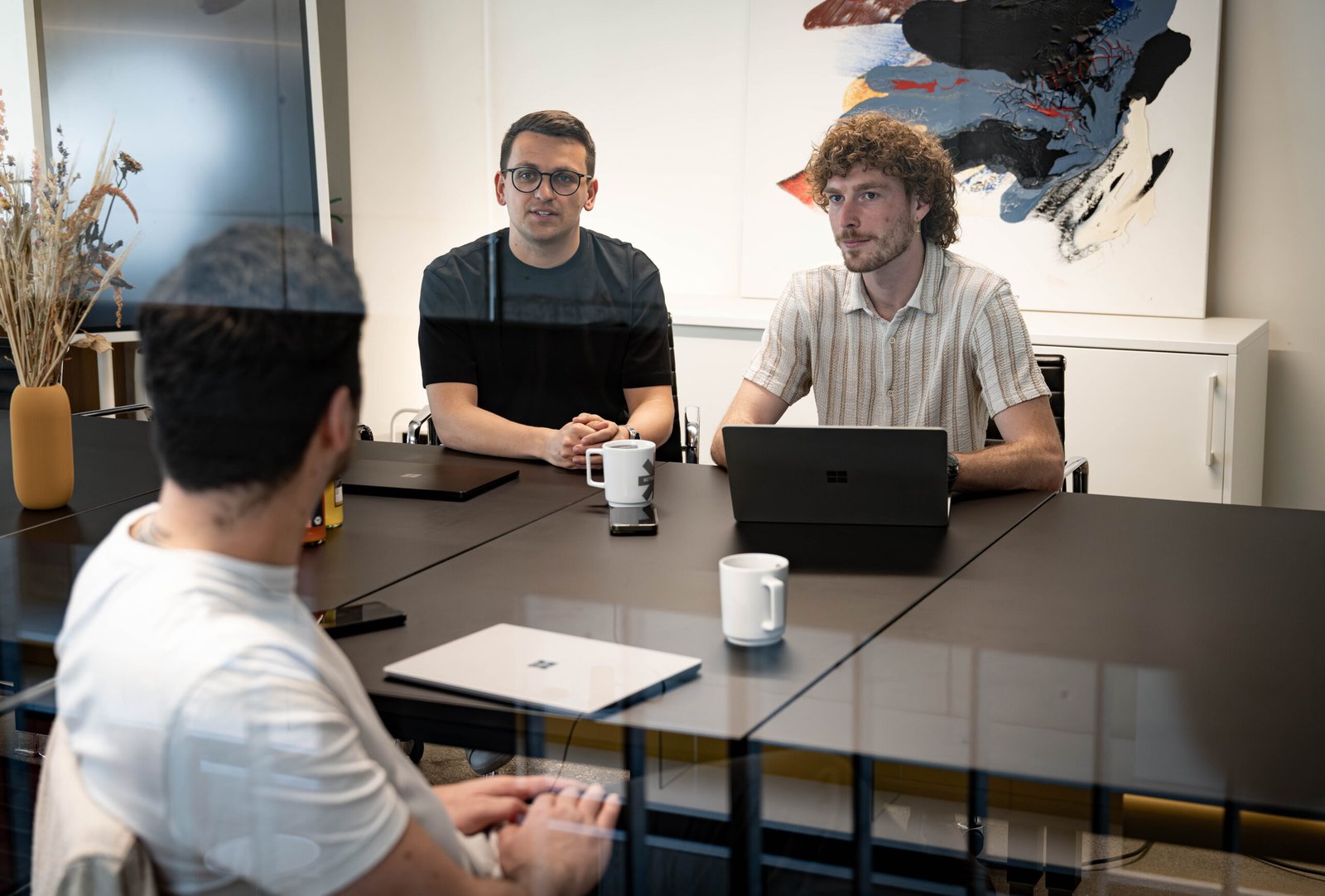 Drei Männer sitzen in einem Meetingraum und unterhalten sich.